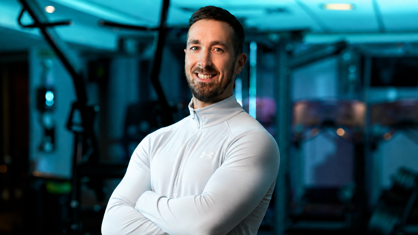 Man in a white athletic jacket standing in a gym with arms crossed